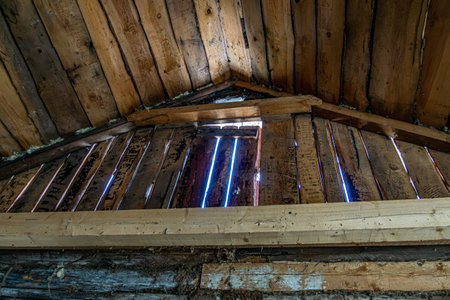 Close up view of an old wooden attic wall showing weathered planks with visible gaps. Daylight streams through the cracks, revealing the aged texture and rustic construction of the structure.の写真素材