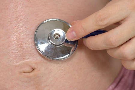 Belly of pregnant woman and hand of doctor with a stethoscopeの写真素材