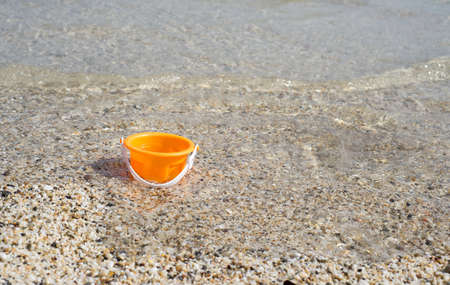 Empty orange toy bucket in the seawaterの写真素材