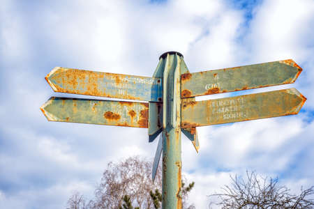 Old rusty street sign with arrows with clouds in backgroundの写真素材