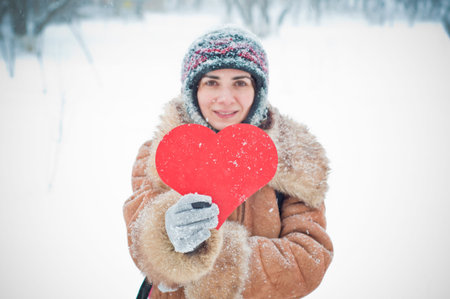 Young woman holding a paper heart while outside is snowing