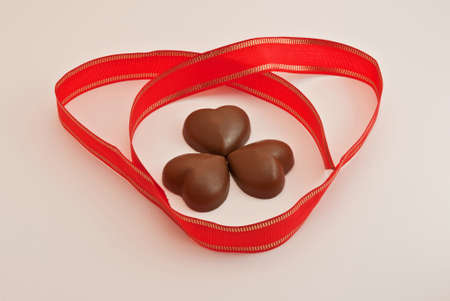Three heart shaped chocolates decorated with a red ribbonの写真素材