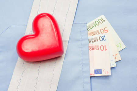 Money in the pocket of a medical uniform, heart and electrocardiogram. Cost of medical service conceptの写真素材