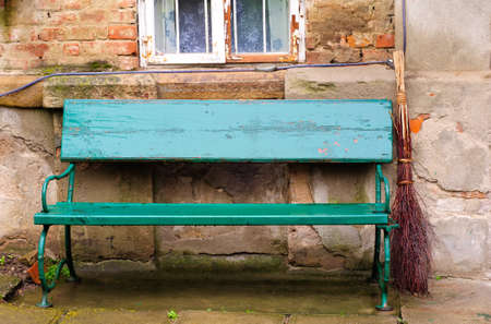 Vintage green bench and broom in front of an old houseの写真素材