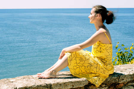 Beautiful young woman sitting on a parapet and admiring the seaの写真素材