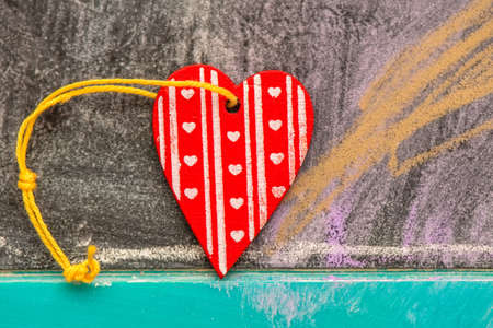 Red wooden heart with yellow string on a chalkboardの写真素材