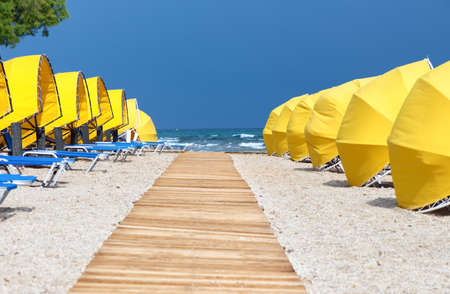 Wooden walkway, umbrellas and sunbeds on the beachの写真素材