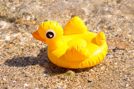 Yellow inflatable duck on the beach near the sea