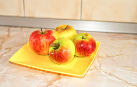 Four apples on a yellow plate on an empty tableの写真素材