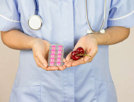 Woman doctor holding pink pills and cherriesの写真素材
