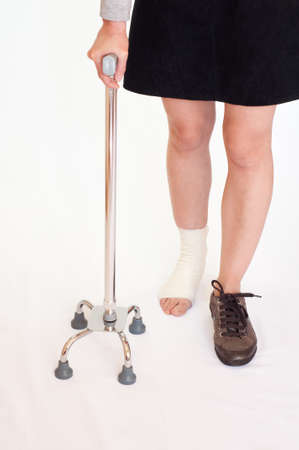 Woman with an injured leg holding a quad stick, isolatedの写真素材