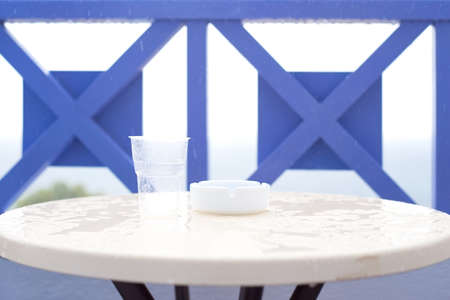 Plastic glass and ashtray on a table during the rainの写真素材