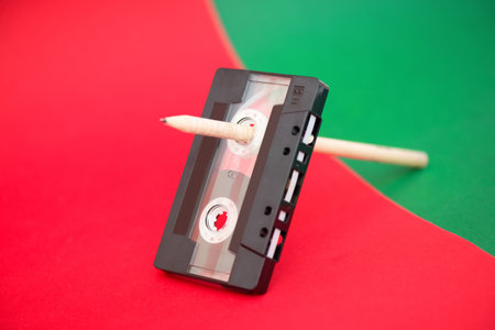 Vintage audio cassette with magnetic band and wooden pencil on red and green backgroundの写真素材