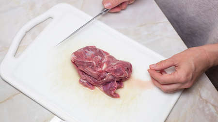 Hands of a woman with knife ready to cut a piece of raw meatの写真素材