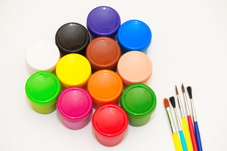 Paintbrushes and gouaches of different colors on white background