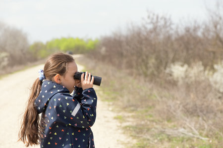 Little caucasian girl looking through binoculars outdoorの写真素材