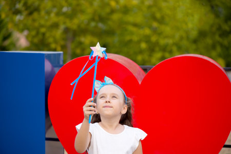 Little girl with magic wand outdoors near a red heart shapeの写真素材