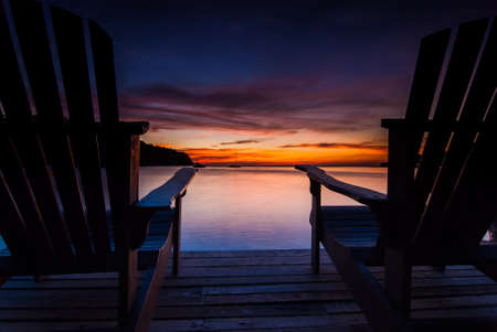 Beach chairs on a wooden bridge with sunsetの写真素材