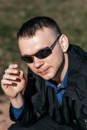 A young man in dark glasses is resting on a bench. A businessman in a stylish raincoat takes off his sunglasses.の写真素材