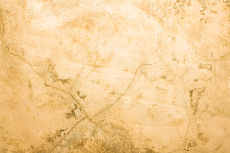 A concrete wall with scuffs and cracks of yellowed color. Yellow background with cement texture.