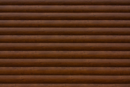 The wall is made of horizontal wooden beams of brown color. Wooden texture. Brown background.