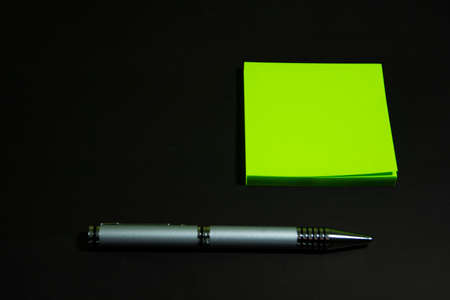Green stickers and a silver ballpoint pen lie on a matte black surface. Stationery on a black table.の写真素材