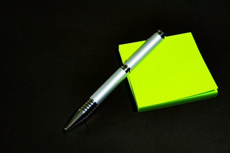 Green stickers and a silver ballpoint pen lie on a black matte surface. Stationery on a black table.