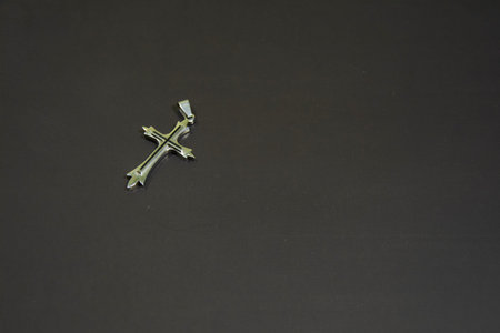 Silver jewelry cross on a black background. Decorations on a black matte surface.