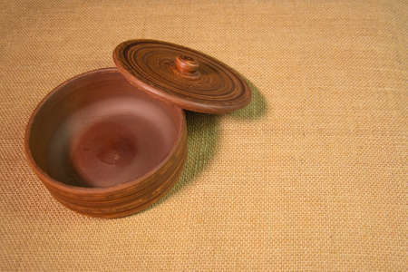 An empty clay vase with a lid on a table covered with burlap. Brown pottery on the table.の写真素材