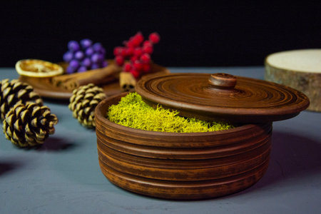 A brown clay pot with yellow moss, covered with a lid and decorative items on a concrete surface. Clay decor on a black background. Decorative dishes of brown color.の写真素材
