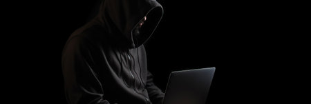 Hacker without face in a hood holds a laptop. on a dark background. Banner for cyber security. Internet web hack technology. Digital laptop in hacker man hand isolated on black. Generate AI.の素材