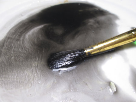 A paintbrush rests in a pool of swirling black and white paint, highlighting the dynamic movement and blending of colors as the artist engages in the creative process.の写真素材