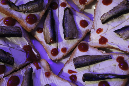 Slices of bread are laid out with a spread of cream cheese topped with pieces of fish and ketchup...