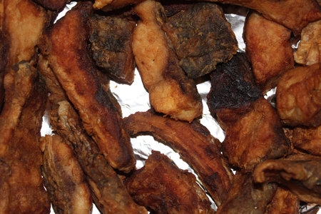 A colorful assortment of crispy fried fish and meat snacks is displayed on a shiny silver surface,...