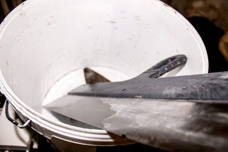 A substantial metal blade is placed diagonally in a white bucket that sits on a workbench, surrounded by tools and a cluttered workshop atmosphere.の写真素材