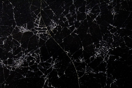 A dark surface features a network of cracks that resemble a complex web, highlighting the intricate...