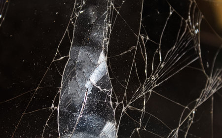 A close-up view reveals a cracked glass surface with intricate patterns and reflections of light,...