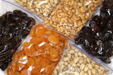 A colorful assortment of nuts and dried fruits in clear bags, including cashews, apricots, and...