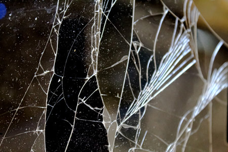 A fractured piece of glass reveals complex cracks and interesting patterns, catching light in a dark...