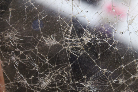 A cracked glass surface showcases a detailed network of fractures and scratches illuminated by...