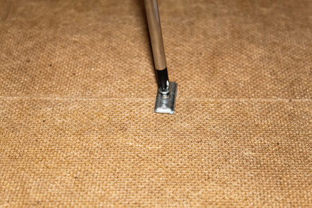 The metal tool lies flat against the burlap, ready for use in crafting, showcasing intricate details of the fabric and tool design.の写真素材