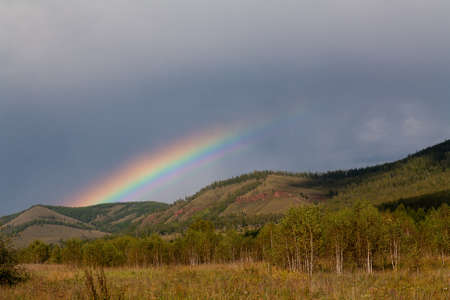 Bright rainbow over mountains and forest against the background of a dark cloud after rainの写真素材