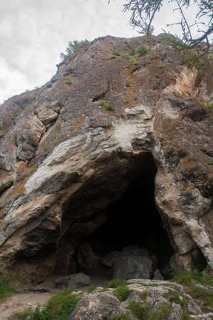 Dark cave entrance made of large gray stones in the mountainsの写真素材