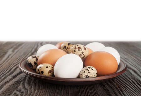 Quail and chicken eggs in a clay plate on a wooden tableの写真素材