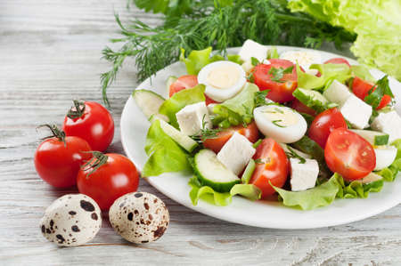 Fresh salad with quail eggs, cherry tomato, cucumber and lettuce on a wooden table.の写真素材