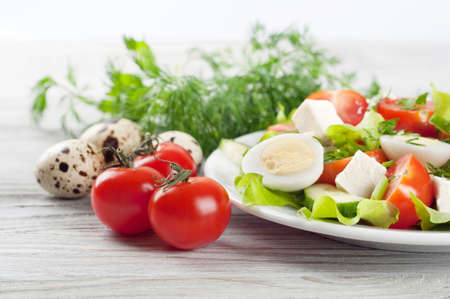 Fresh salad with quail eggs, cherry tomato, cucumber and lettuce on a wooden table.の写真素材