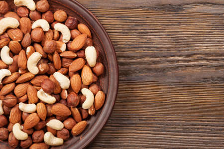Different nuts in plate on a wooden background. Almond, hazelnut and cashew.の写真素材