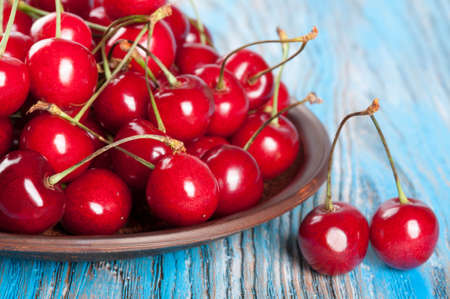 Red sweet cherry in a clay dish on a blue wooden backgroundの写真素材