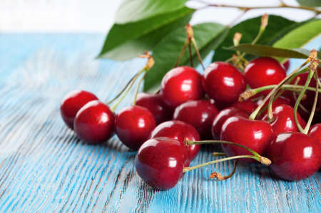 Red sweet cherry and green leaves on a blue wooden backgroundの写真素材