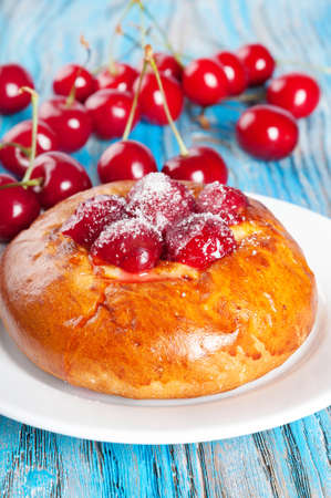 Fresh homemade bun with sweet cherry on a blue wooden backgroundの写真素材
